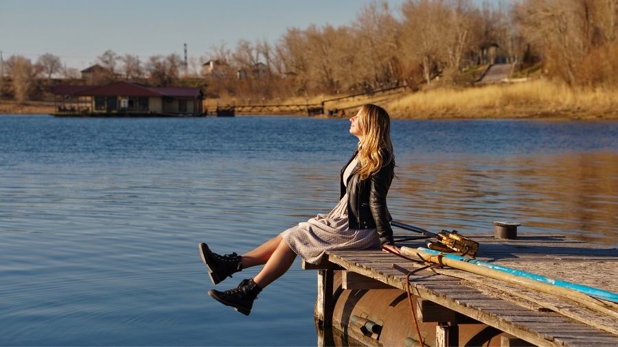 Woman sitting on a bridge with her eyes closed and a gentle smile, appearing happy.