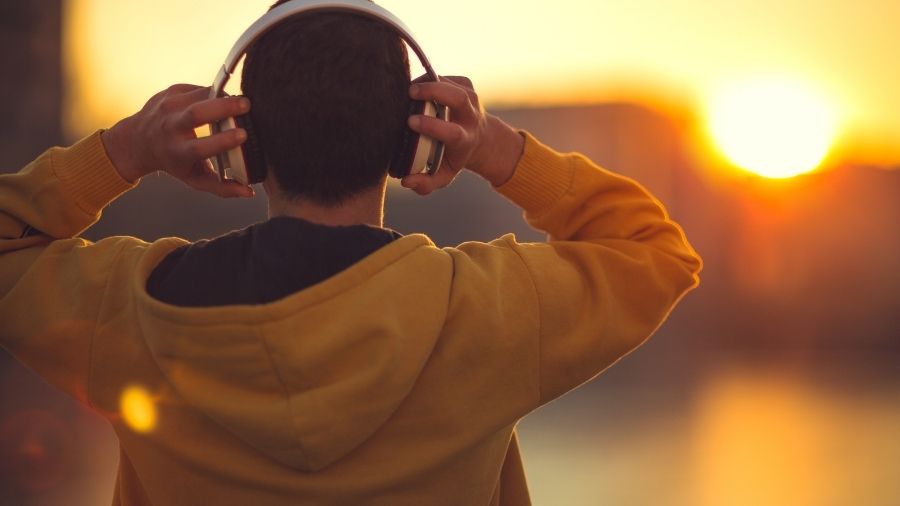 Man wearing a yellow jumper, listening to positive music with headphones on while enjoying the sunshine.