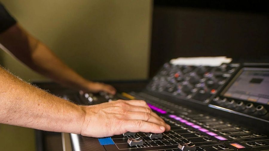 Man’s hand adjusting controls for multitrack recording, in focus.