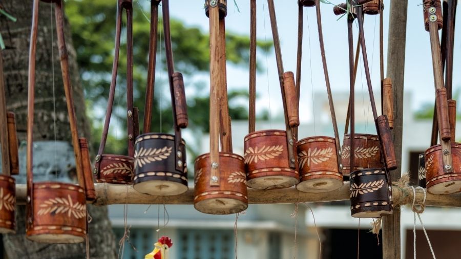 A selection of hand-carved wooden Ektara stringed instruments hanging on a bamboo cane outside, showcasing their unique designs.