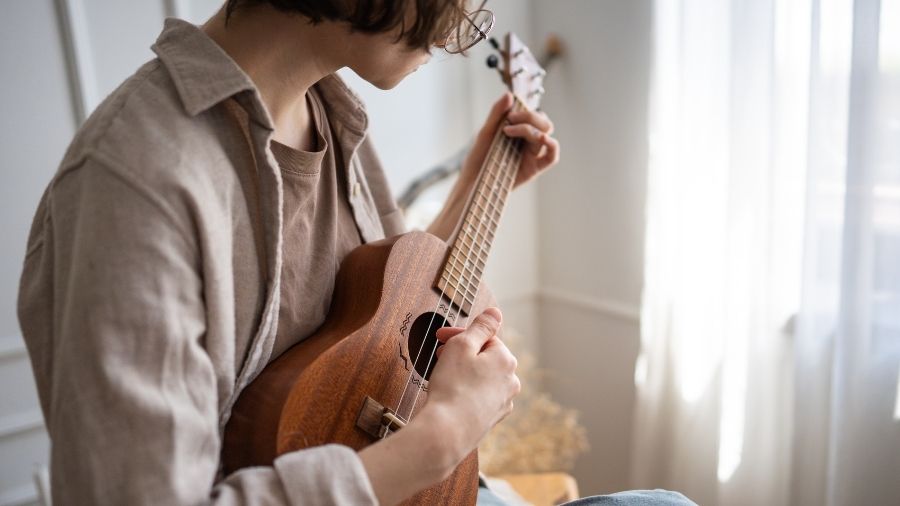 Young woman rehearsing ukulele chords at home, refining finger placement and strumming technique.