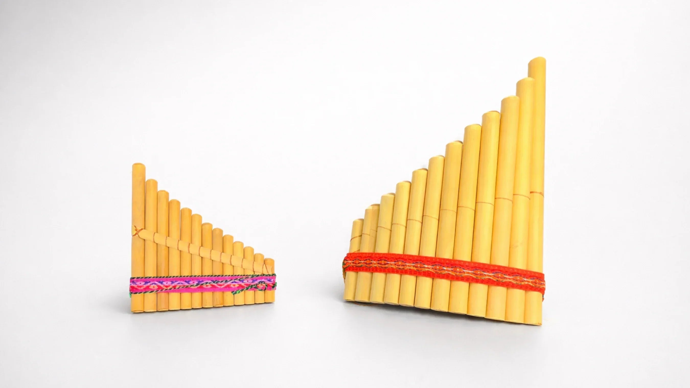 small Antares pan pipes with pink ribbon next to larger Siku pan pipes