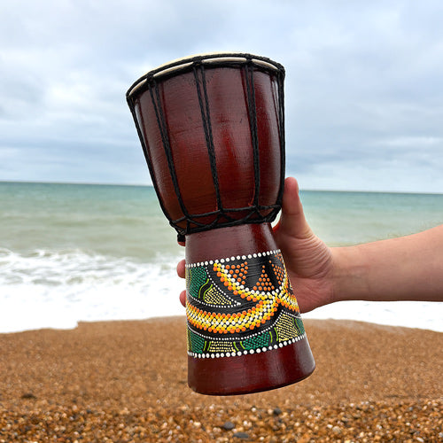 Decorative drum held by a hand on a beach with ocean in the background