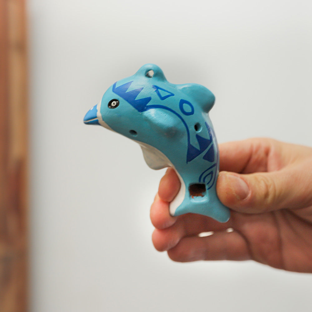 Close-up of a ceramic blue dolphin design ocarina held in hand to show its size and scale.