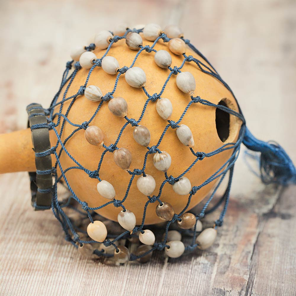 Close-up of the gourd Cabassa shaker showing the shells on the netted bag, the gourd body, and the wooden handle.