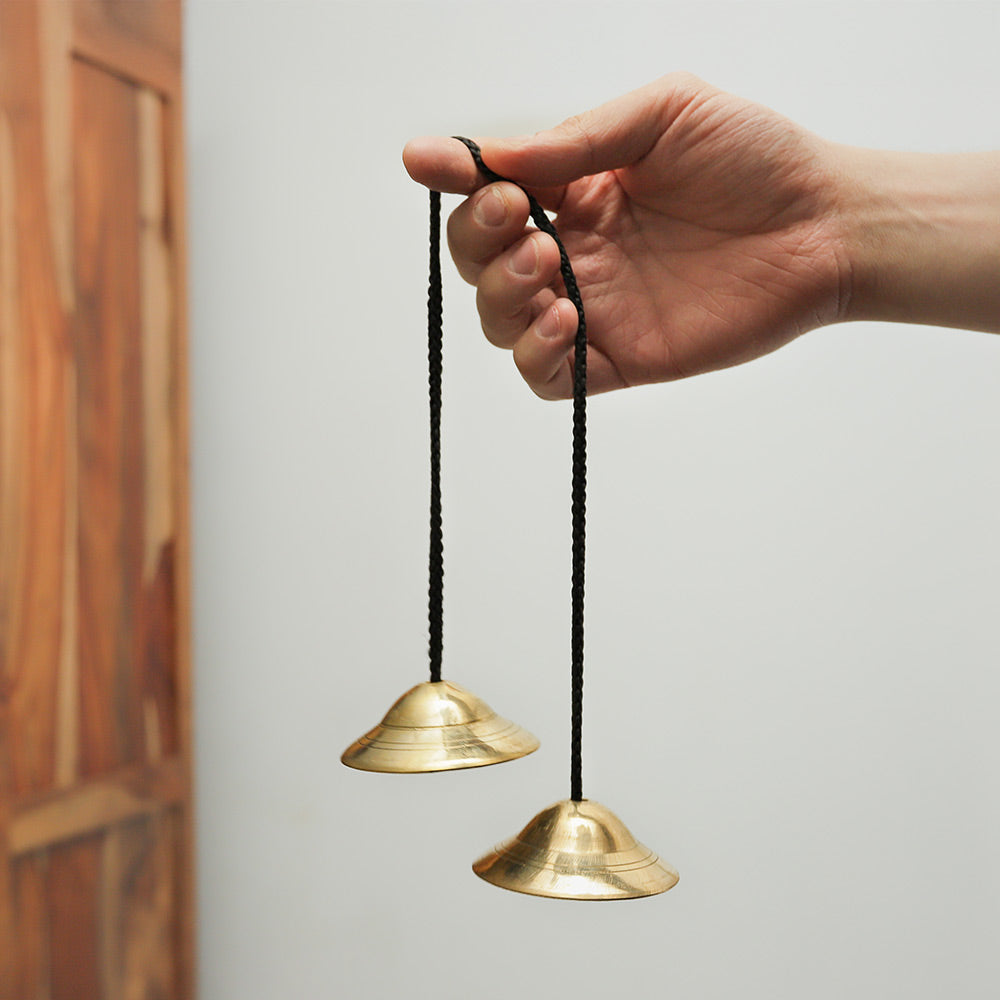Indian Manjira brass prayer bells held in the hand to demonstrate the size and length of the instrument.