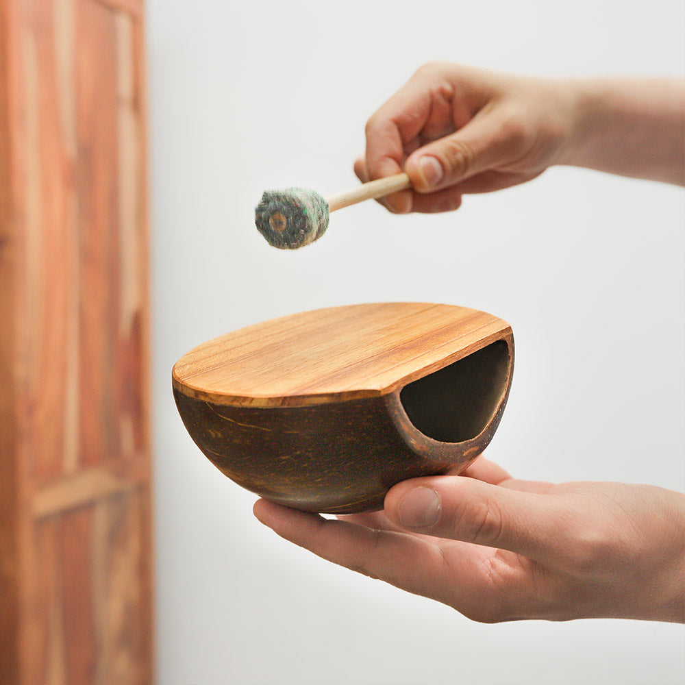 Coconut drum held in hand with a beater, demonstrating its size and design.