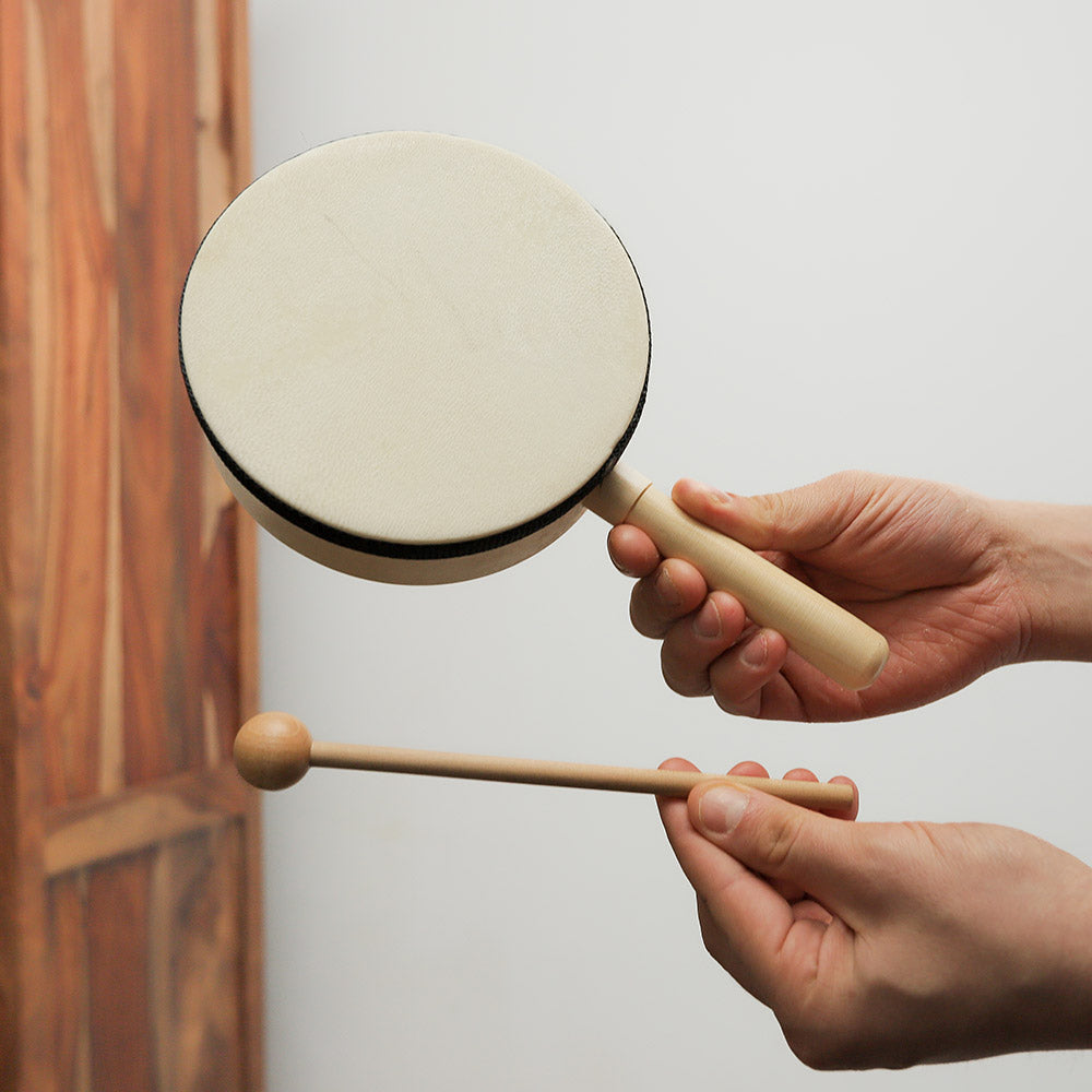 Karo drum held in hand alongside its beater, showing the size and how it is played.