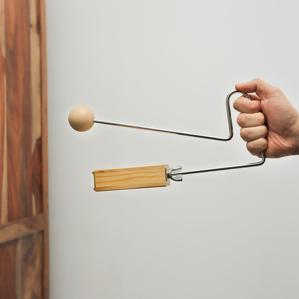 Light brown vibraslap instrument held in hand, demonstrating its size and how to hold it.