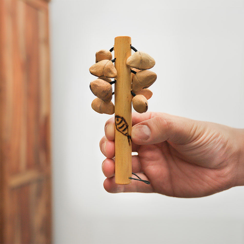 Lima Kenari stick shaker with natural seeds and a wooden handle, featuring a carved fish design, held in hand for scale.