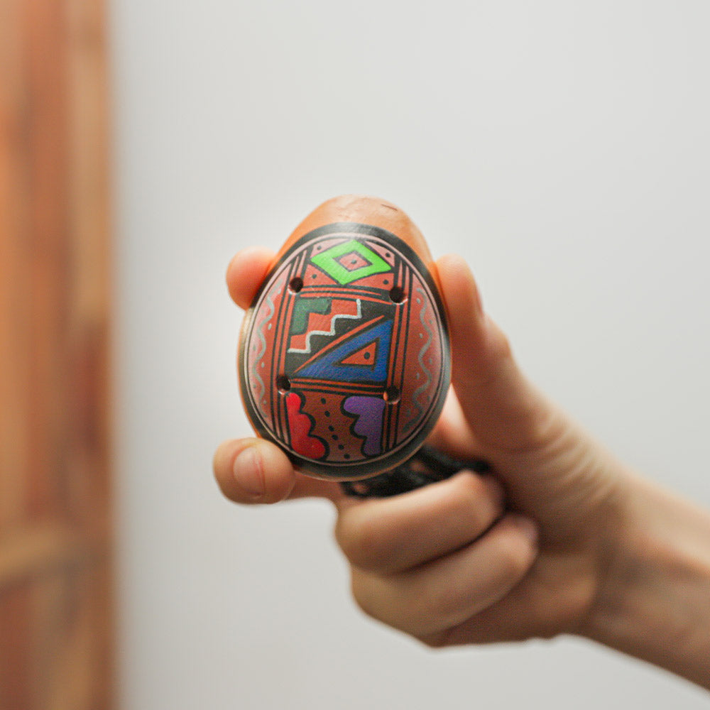 Pendant ocarina instrument held in the hand to show scale and size, with finger holes and string visible.