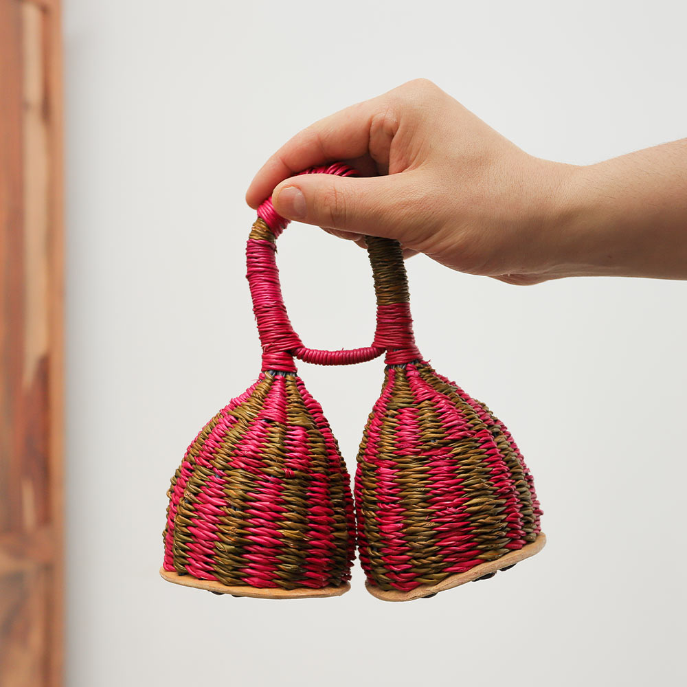 Colourful pink straw double caxixi shaker, a traditional African percussion instrument, handheld for scale.