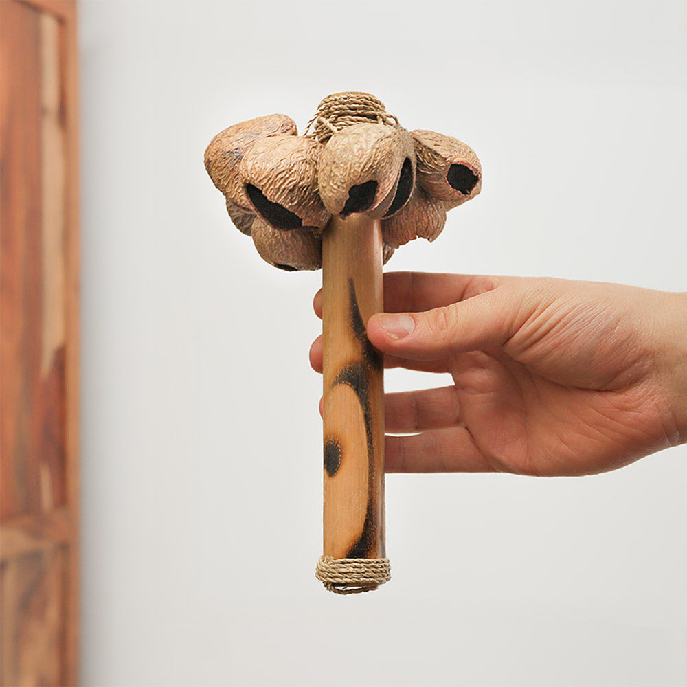 Handheld Raha Stick shaker made from natural seed husks with a bamboo handle, used for percussion and sound therapy.