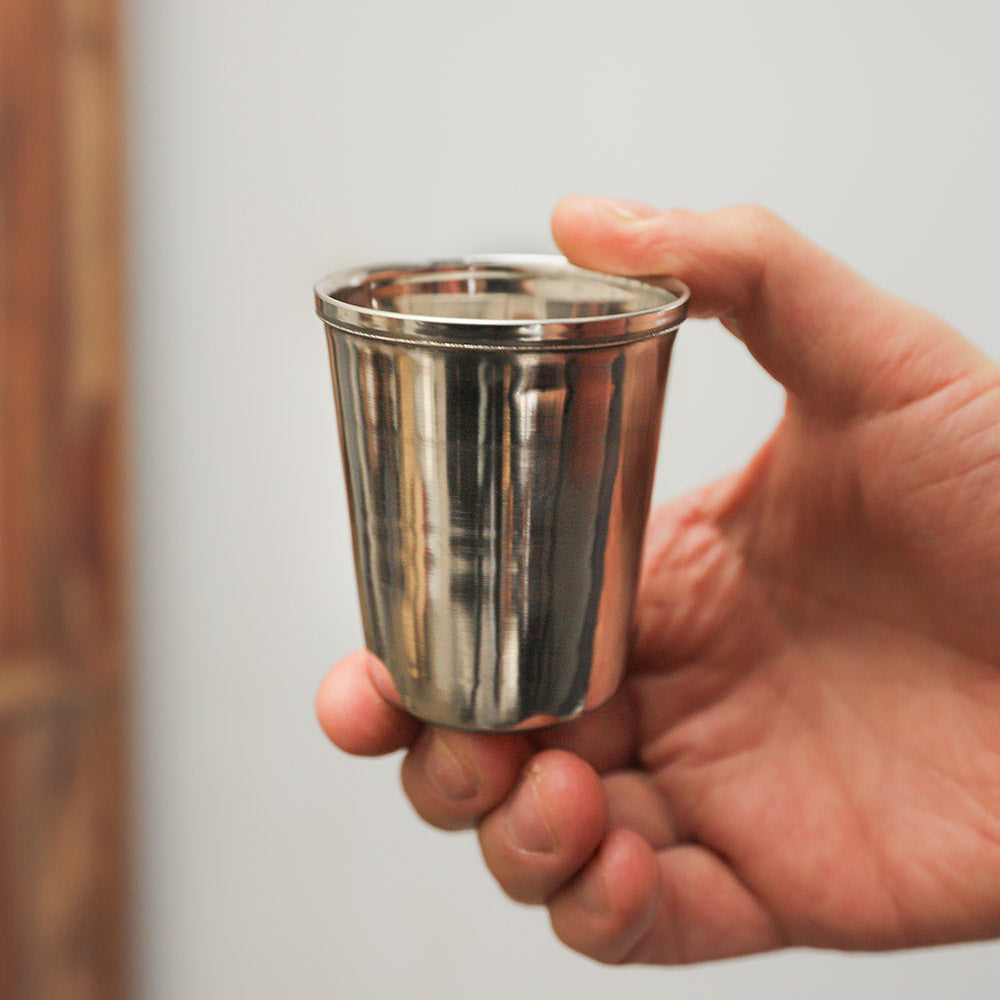 Stainless steel ringing cup shaker instrument, held in hand to show scale.