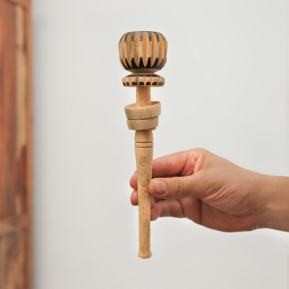 Traditional Mexican molinillo whisk made of solid wood, held in hand for scale, showcasing its size and carved details.
