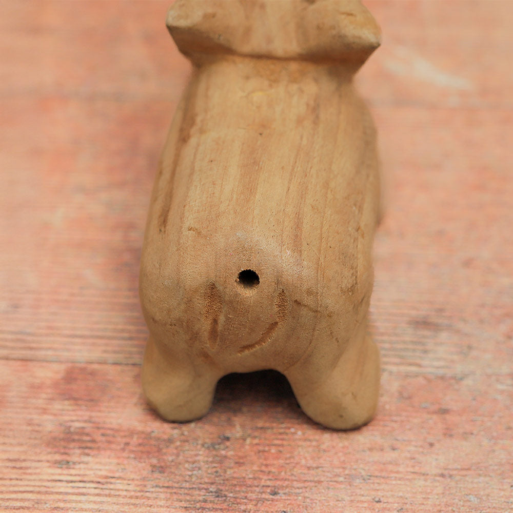 Close-up of the wooden pig whistle's rear end, showing the whistle hole used for blowing.