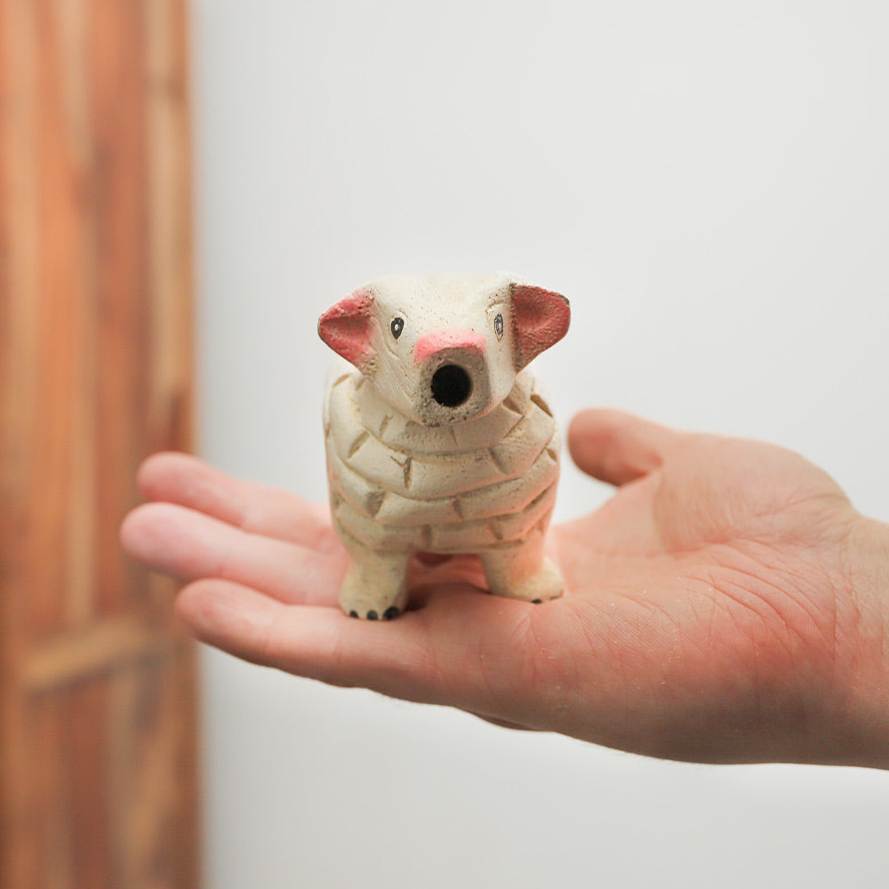 Wooden sheep whistle held in hand, showing its size, face and carved design.