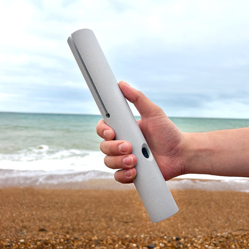 Hand holding a kutuwapa on a beach with ocean and sky in the background