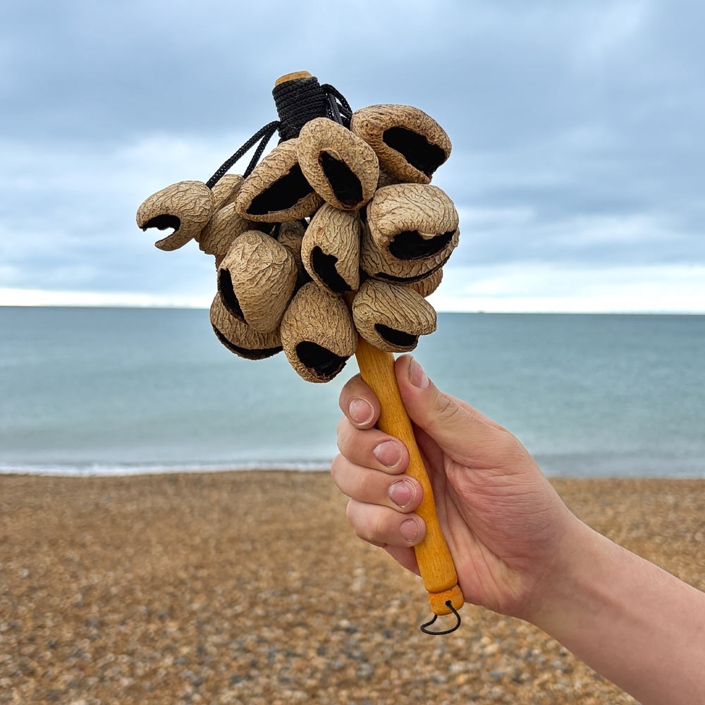 Hand holding a wooden pangi stick cluster on a beach with ocean and sky in the background