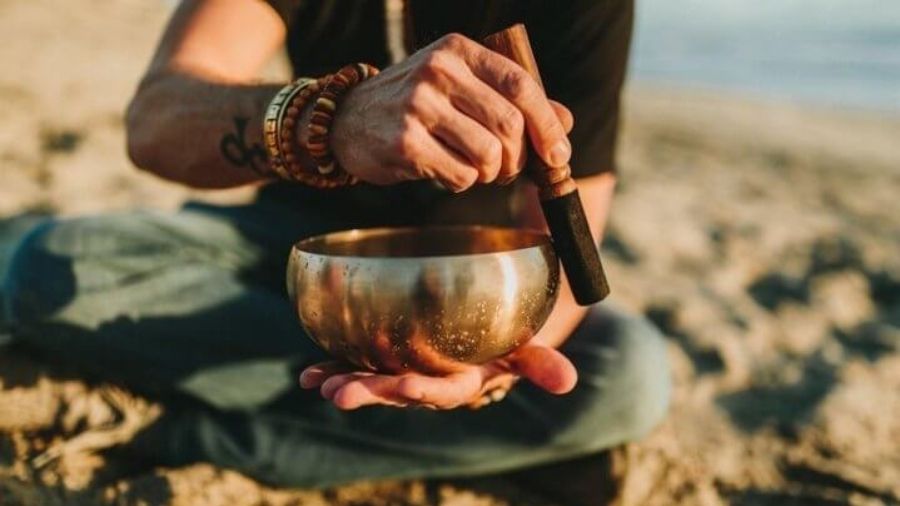 A person holding a singing bowl with mallets and strikers, attempting to create a smooth, circular ringing sound
