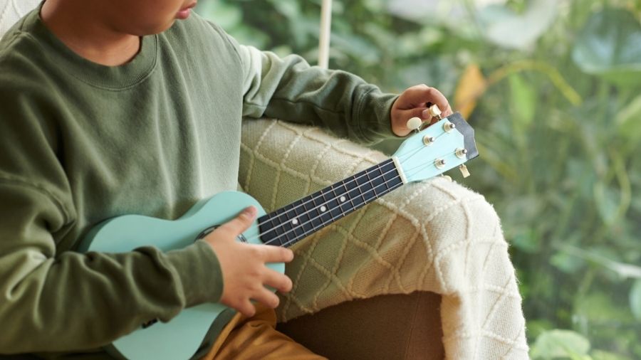 A boy in a green sweater tuning his ukulele.