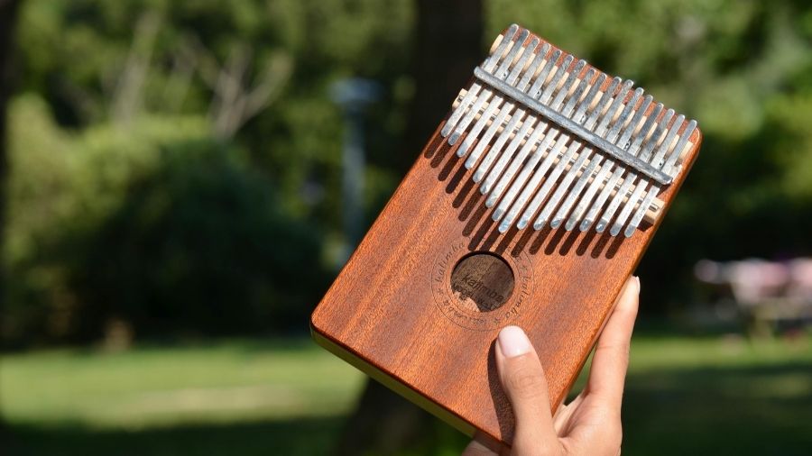 A hand holding a wooden kalimba outdoors, with natural light highlighting the instrument.