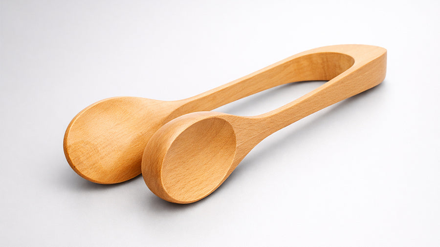 Polished wooden spoon tongs made from light natural wood, displayed on a smooth warm grey satin background with soft shadows highlighting the curved ergonomic design and fine wood grain texture