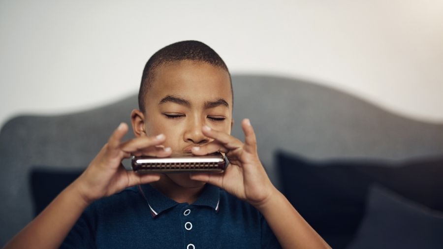 Boy playing a harmonica, in focus, with a blurred background.