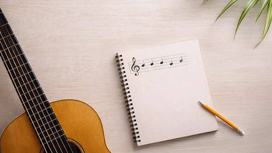 Beginner music theory notebook with written musical notes next to an acoustic guitar on a wooden desk, representing learning notes, chords, and melody fundamentals
