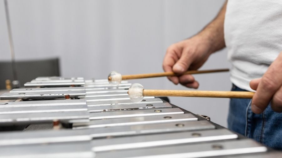 A person playing a glockenspiel with mallets, striking the metal bars to create bright tones.