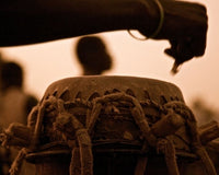 Silhouette of a person playing a Djembe drum and carefully tending to the instrument.