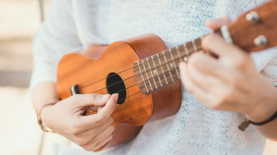 Person holding a wooden ukulele and plucking