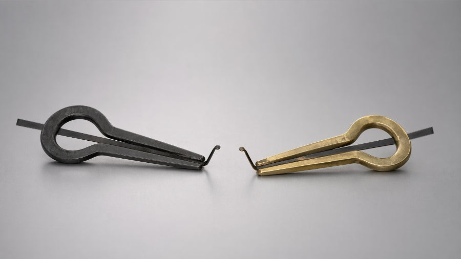 Cast iron and brass jaw harps side by side on a grey studio background