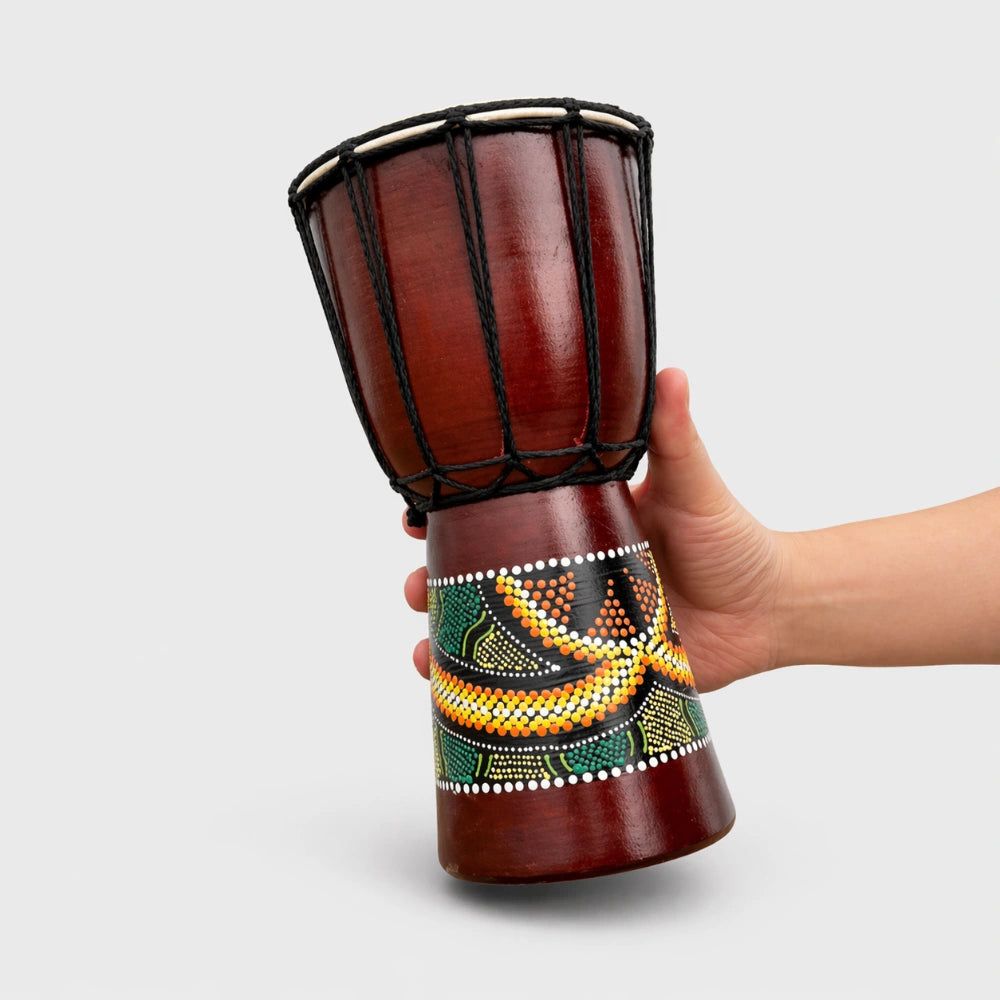 Decorative drum held by a hand on a beach with ocean in the background