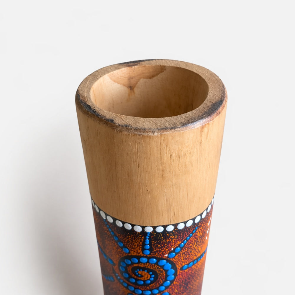 Close up of the wooden Melaya didgeridoo showing open blowing end and spiral dotted hand painted design on a white background