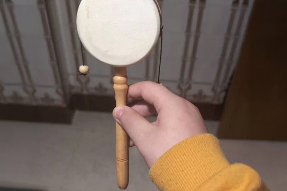 Hand holding a small monkey drumwith a wooden handle against a neutral background