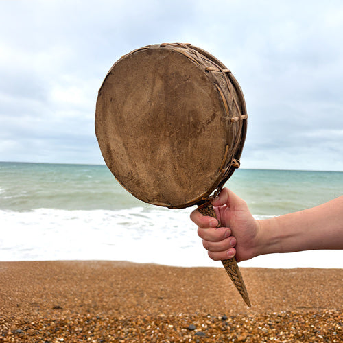 Hand holding a brown drum against a beach background