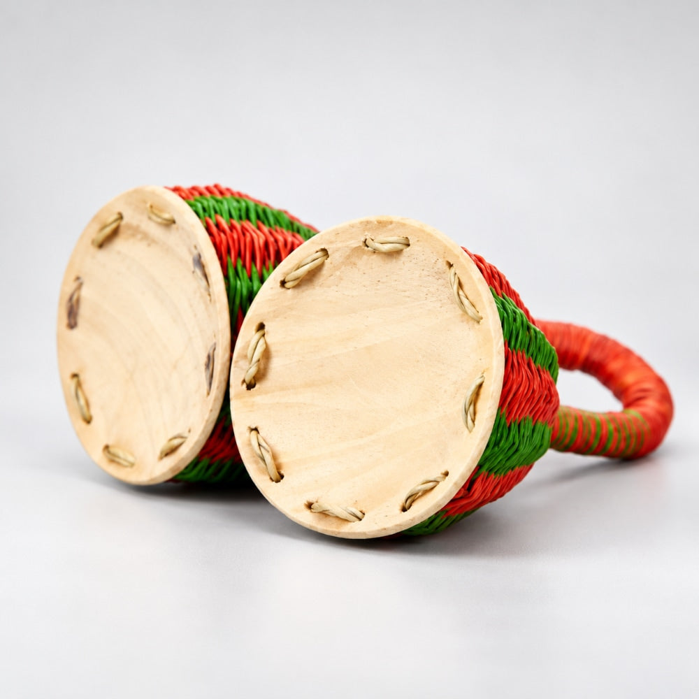 Underneath the double caxixi shaker with red and green wrapped baskets, photographed on a clean light gray studio background.