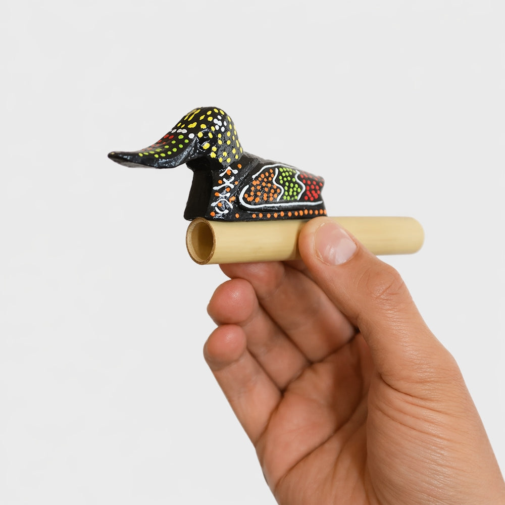 Hand holding a smal, intricately designed wooden duck quacker whistle with a plain studio background