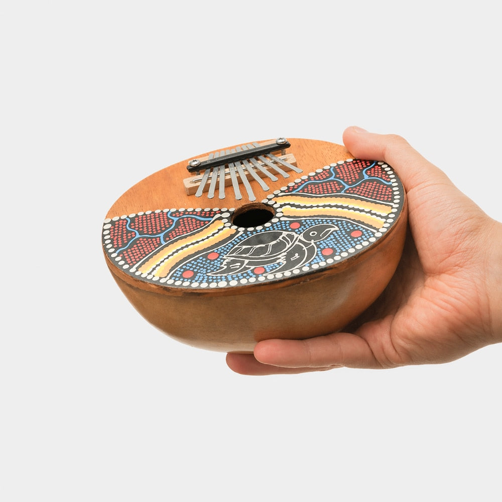 Hand holding a decorated gourd thumb piano kalimba with 9 notes and dot painted design on a white studio background