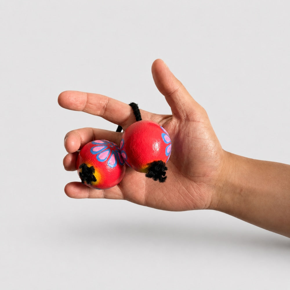 Hand holding floral painted kashaka shakers showing scale and how to play