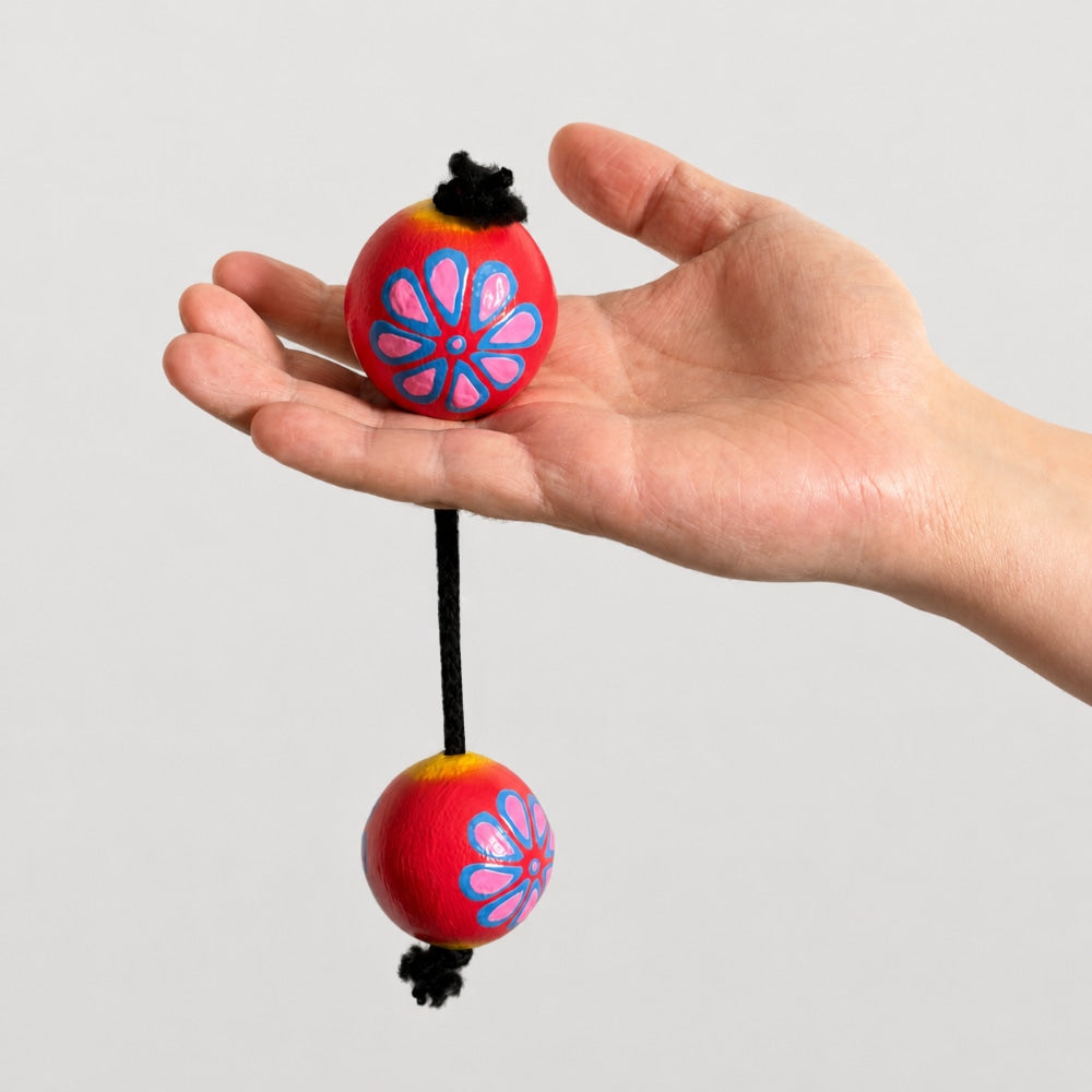 Floral painted kashaka shaker held in hand to show scale with a light grey studio background