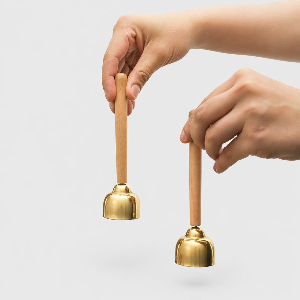 Two hands holding brass handbells against a light gray background