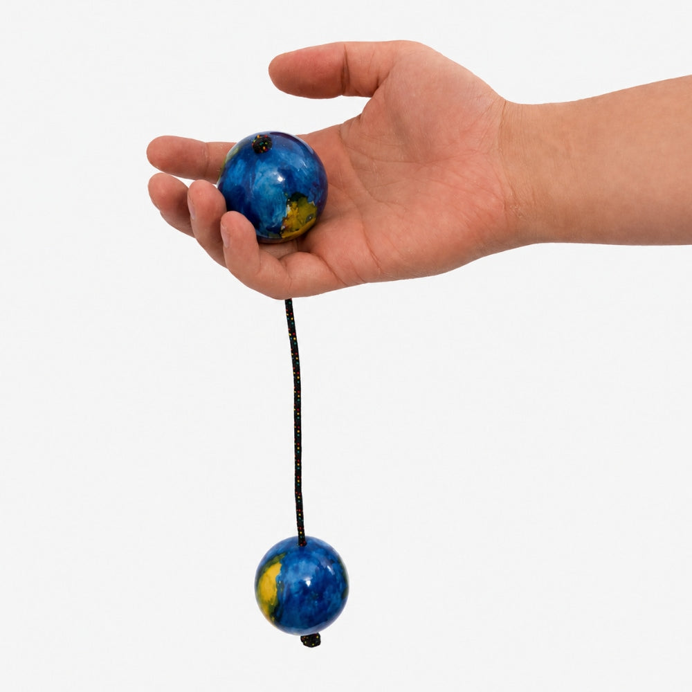 Hand holding a blue and yellow kashaka ball with a string against a white background