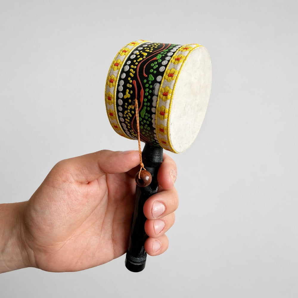 Hand holding a colorful hand drum against a plain background