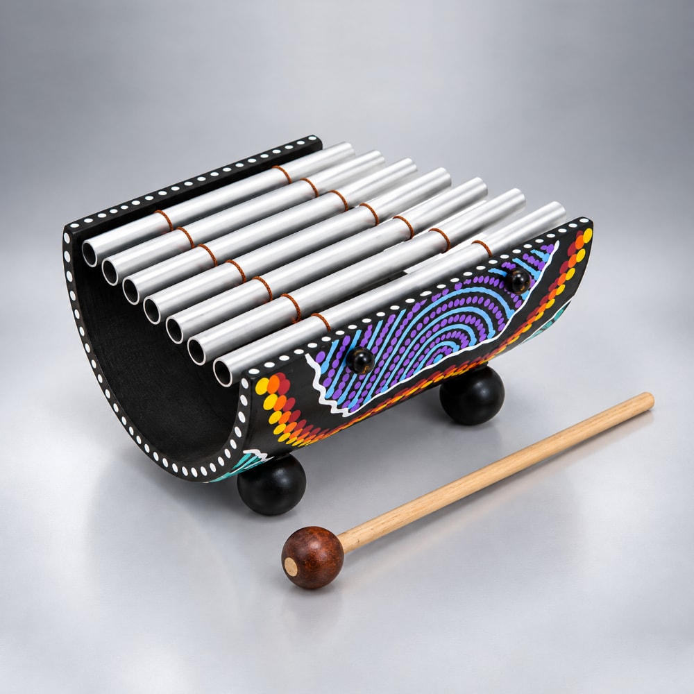 A handcrafted wooden 7 note indonesian dot painted gamelan with silver metal tubes, decorated with colorful painted patterns on the sides, resting on wooden feet with a wooden mallet in the foreground, set against a neutral gray background.